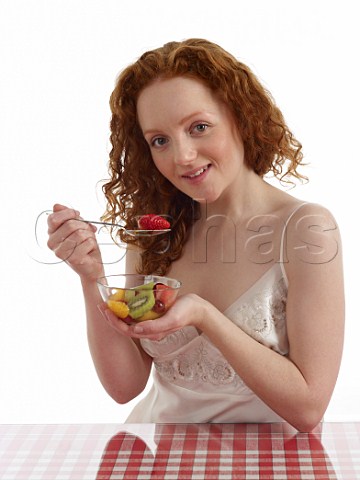 Young woman sitting at breakfast table with bowl of fresh fruit salad