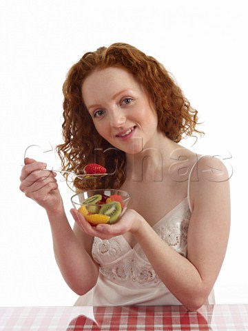 Young woman sitting at breakfast table with bowl of fresh fruit salad