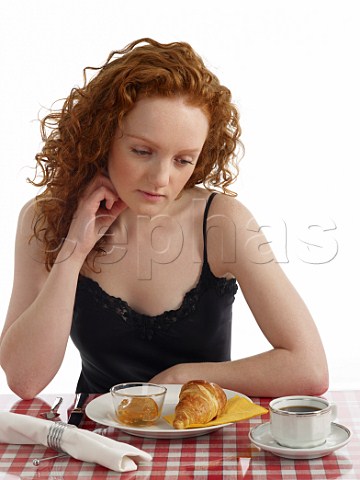 Young woman sitting at breakfast table croissant with marmalade cup of black coffee