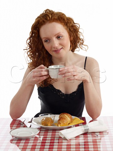 Young woman sitting at breakfast table croissant with marmalade cup of black coffee