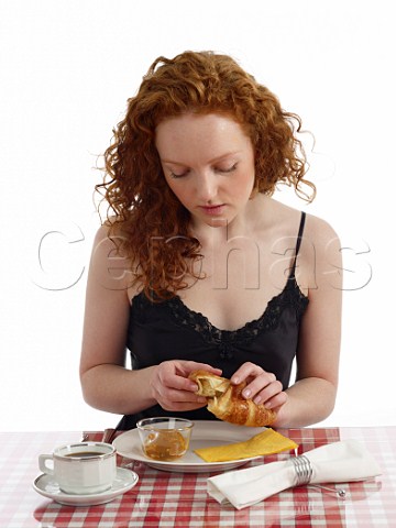 Young woman sitting at breakfast table croissant with marmalade cup of black coffee