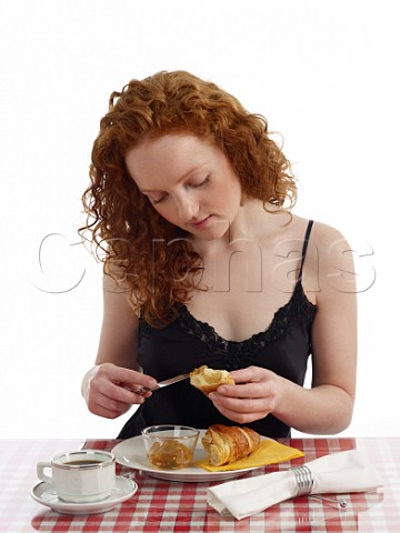 Young woman sitting at breakfast table croissant with marmalade cup of black coffee