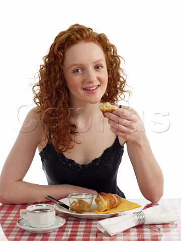 Young woman sitting at breakfast table croissant with marmalade cup of black coffee