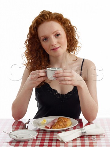 Young woman sitting at breakfast table croissant with ham and butter cup of black coffee