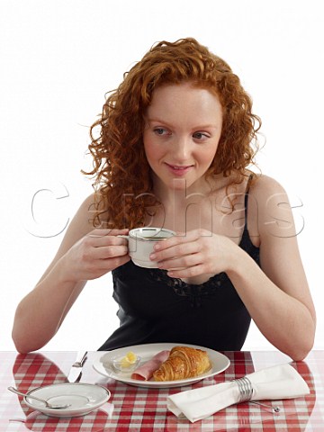 Young woman sitting at breakfast table croissant with ham and butter cup of black coffee