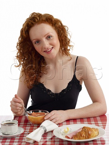 Young woman sitting at breakfast table pink grapefruit croissant with ham and butter cup of black coffee