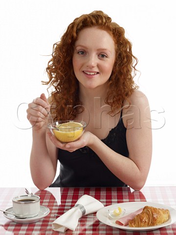 Young woman sitting at breakfast table grapefruit croissant with ham and butter cup of black coffee