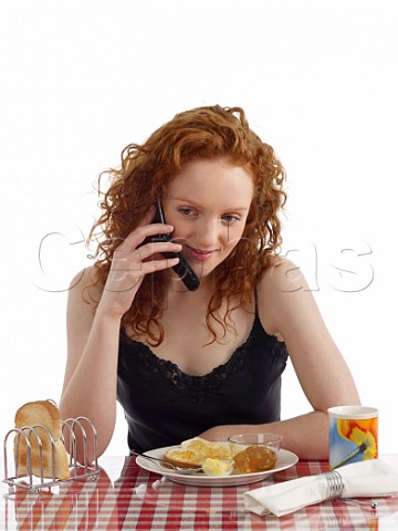 Young woman talking on mobile phone at breakfast table toast and marmalade mug of tea
