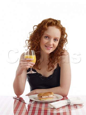 Young woman at breakfast table bagel with ham and cream cheese glass of orange juice