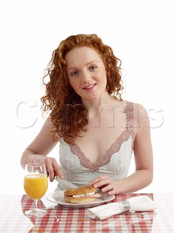 Young woman at breakfast table bagel with ham and cream cheese glass of orange juice