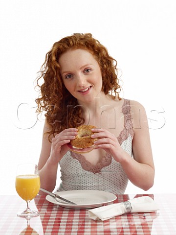 Young woman at breakfast table bagel with ham and cream cheese glass of orange juice