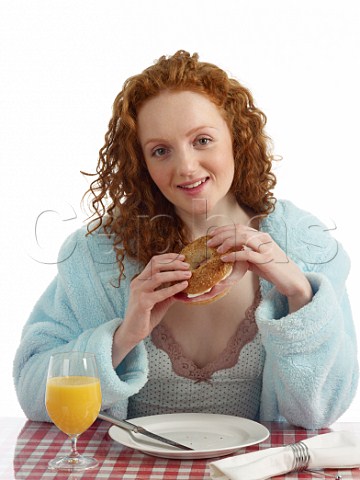 Young woman at breakfast table bagel with ham and cream cheese glass of orange juice