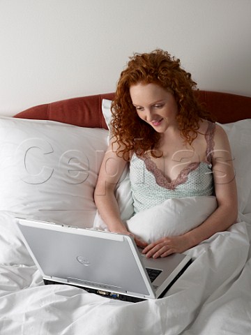 Young woman in bed with laptop computer