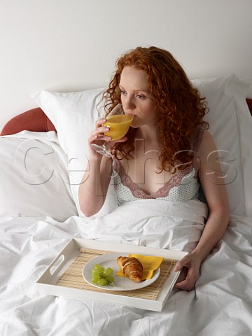 Young woman having breakfast in bed croissant grapes glass of orange juice