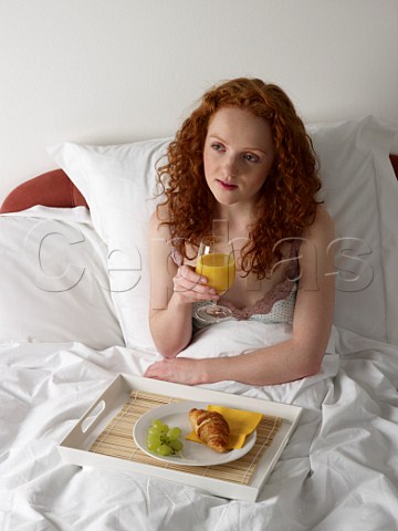 Young woman having breakfast in bed croissant grapes glass of orange juice