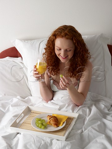 Young woman having breakfast in bed croissant grapes glass of orange juice
