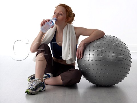 Young woman drinking from bottle of water after workout in a gym