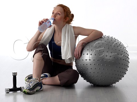 Young woman drinking from bottle of water after workout in a gym