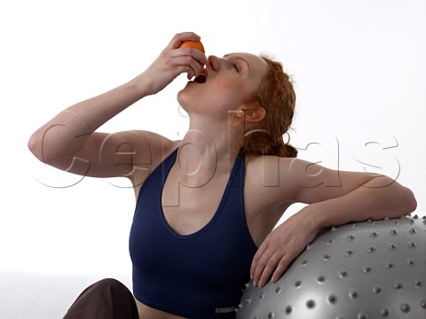 Young woman squeezing juice from half an orange after workout in a gym