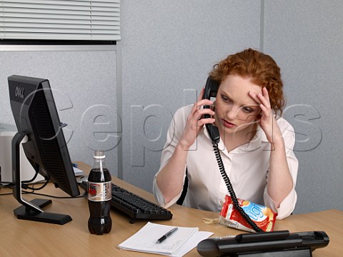 Young woman on telephone at her office desk bottle of diet coke and bag of lofat crisps