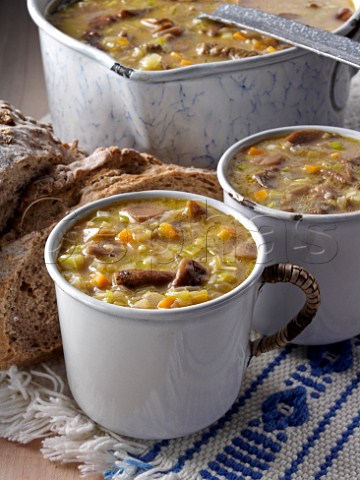 Two mugs of Polish mushroom soup with a saucepan and rye bread