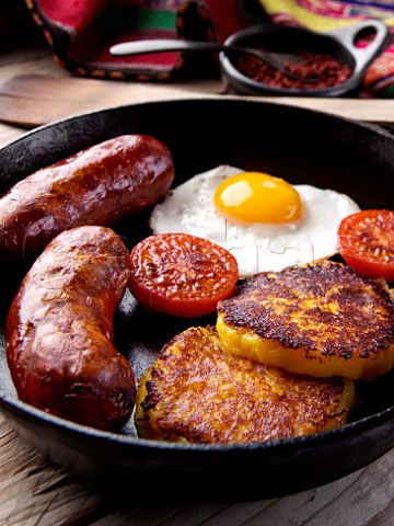 Llapingachos Equadorian cheese and potato patties with fried egg tomato and chorizo sausage in a frying pan