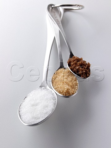 White granulated demerara and dark brown sugar in measuring spoons