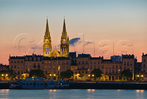 Lights of Quai des Chartrons reflecting in the Garonne river at dusk with the spires of StLouis church behind Bordeaux Gironde France