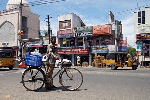 Indian man carrying water containers on a bicycle along a main road Chennai Madras India