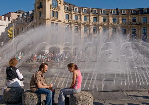 People enjoying warm summer sunshine at Karlsplatz fountain Munich Bavaria Germany