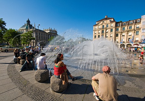 People enjoying warm summer sunshine at Karlsplatz fountain Munich Bavaria Germany