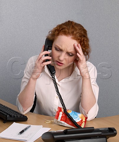 Young woman on telephone at her office desk looking stressed bag of lofat crisps