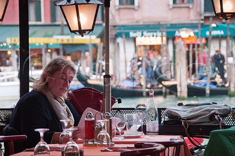 Woman reading menu in openair restaurant seating overlooking the Grand Canal Riva del Vin Rialto Venice Italy