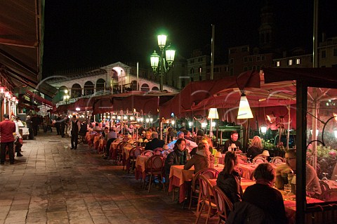 Open air restaurant seating overlooking the Grand Canal at night with Rialto bridge behind Riva del Vin Rialto Venice Italy