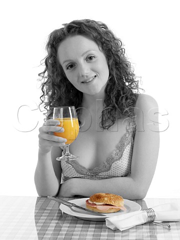 Young woman at breakfast table bagel with ham and cream cheese glass of orange juice