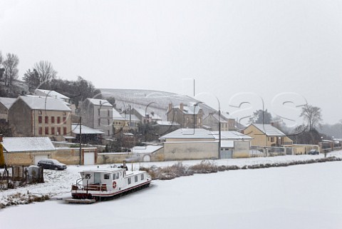 Snow falling on the frozen Canal Latral de la Marne at MareuilsurAy with the Clos des Goisses vineyard of Philipponnat on the hill beyond  Marne France Champagne