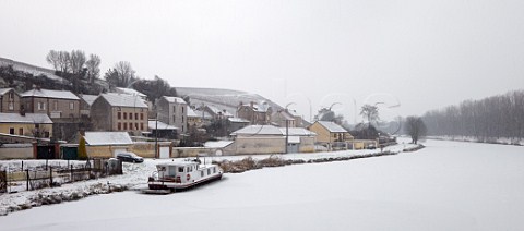 Snow falling on the frozen Canal Latral de la Marne at MareuilsurAy with the Clos des Goisses vineyard of Philipponnat on the hill beyond  Marne France Champagne