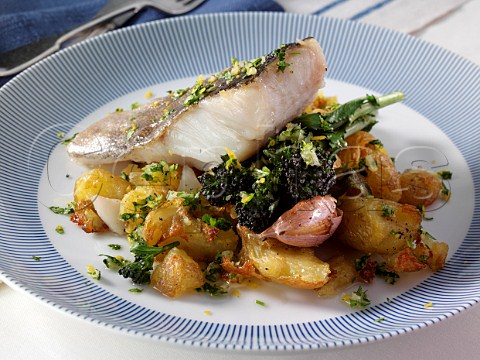 A baked fillet of pollack on a bed of crispy crushed Charlotte potatoes with purple sprouting broccoli sage and garlic and gremolata sauce