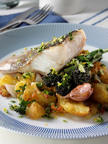 A baked fillet of pollack on a bed of crispy crushed Charlotte potatoes with purple sprouting broccoli sage and garlic and gremolata sauce