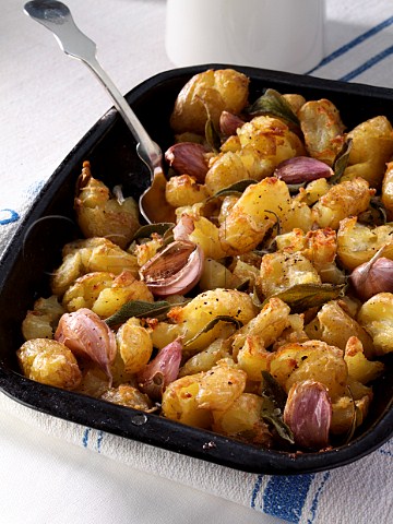 Crispy crushed Charlotte potatoes with sage and garlic in a roasting pan