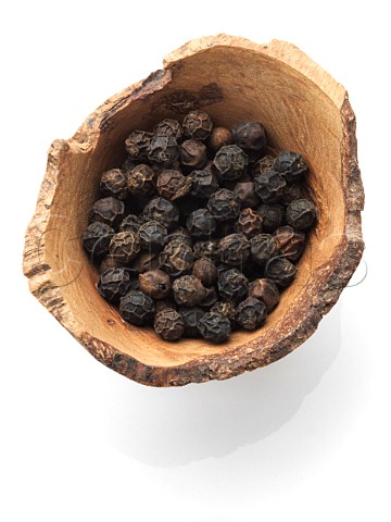 Black peppercorns in a wooden bowl on a white bckground