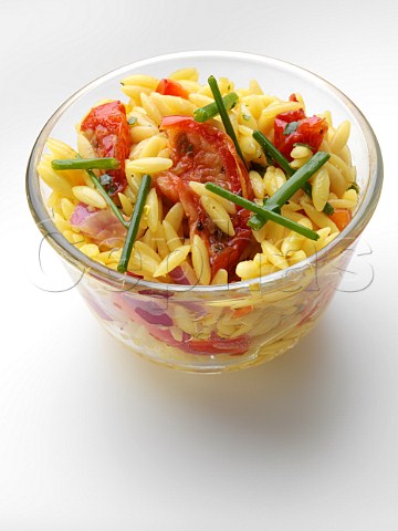 Orzo rice sun dried tomato salad in glass bowl on a white background