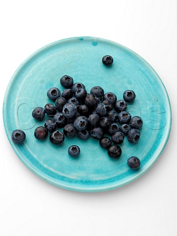 Ripe blueberries on a turquoise plate on a white background