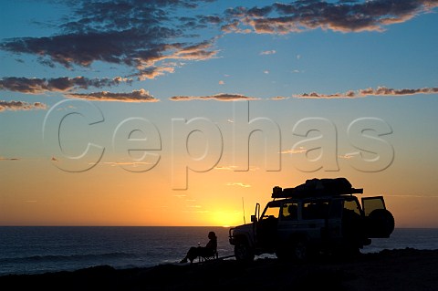 Woman with glass of wine by 4WD vehicle  sunset over the Southern Ocean Nullarbor National Park South Australia