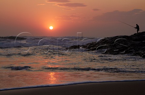 Sunrise over the Indian Ocean with man fishing from the rocks Amanzimtoti KwaZuluNatal South Africa