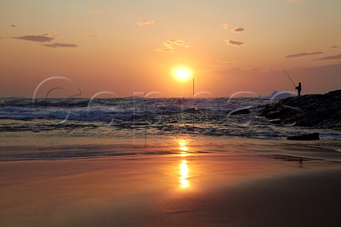 Sunrise over the Indian Ocean with man fishing from the rocks Amanzimtoti KwaZuluNatal South Africa