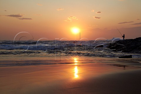 Sunrise over the Indian Ocean with man fishing from the rocks Amanzimtoti KwaZuluNatal South Africa