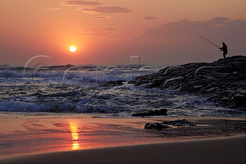 Sunrise over the Indian Ocean with man fishing from the rocks Amanzimtoti KwaZuluNatal South Africa