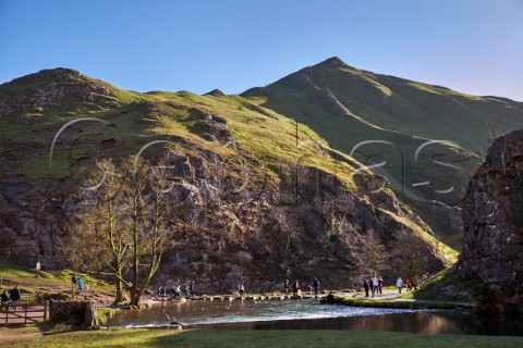 People on the famous Stepping Stones across the River Dove in Dovedale with Thorpe Cloud beyond Ilam Derbyshire England Peak District National Park