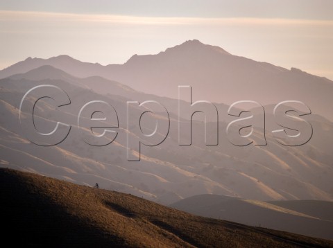 Mountain biker riding a ridge in the Wither Hills with the Blairich Range beyond Marlborough New Zealand